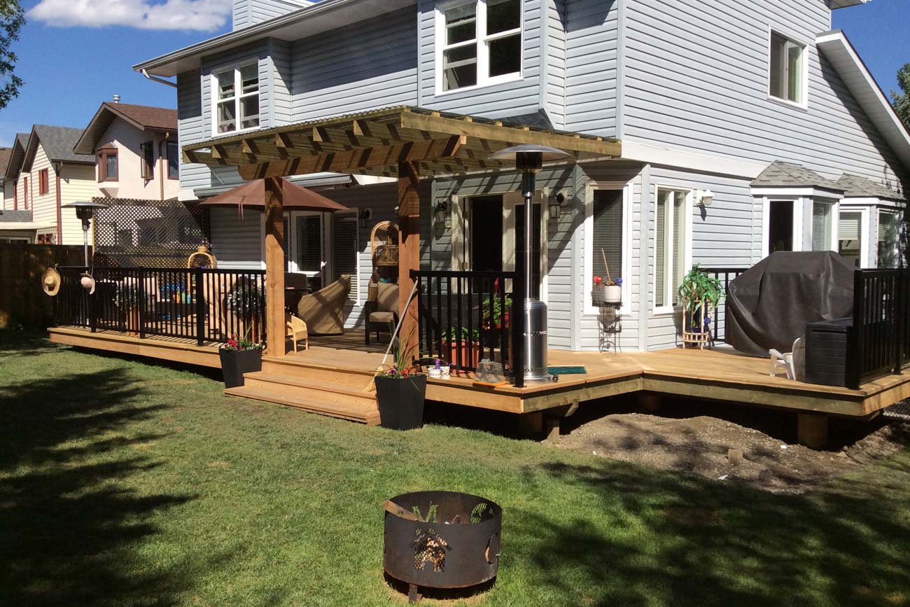 a photo of a backyard with a fire pit, wooden deck and pergola