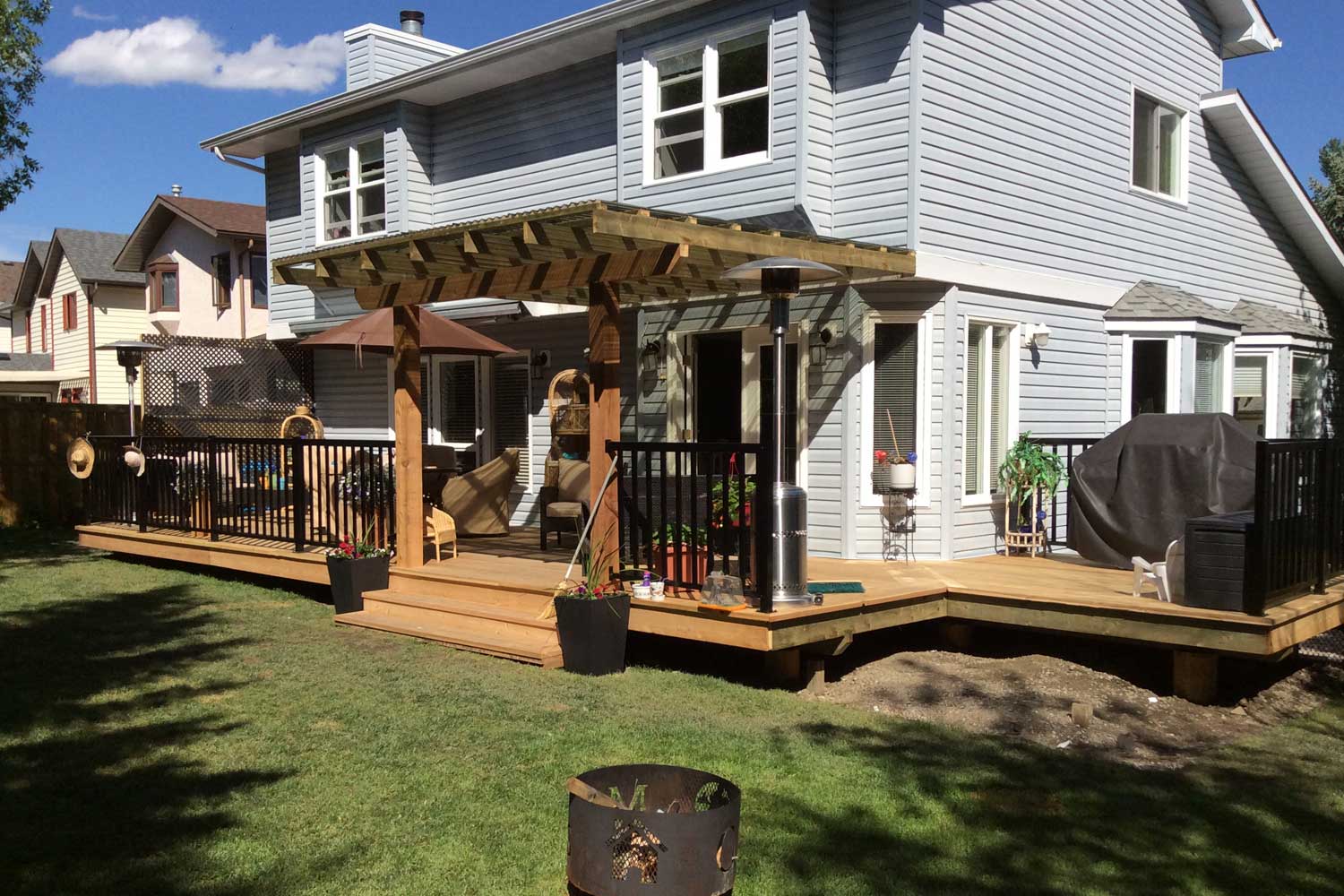 a photo of a backyard with a fire pit, wooden deck and pergola